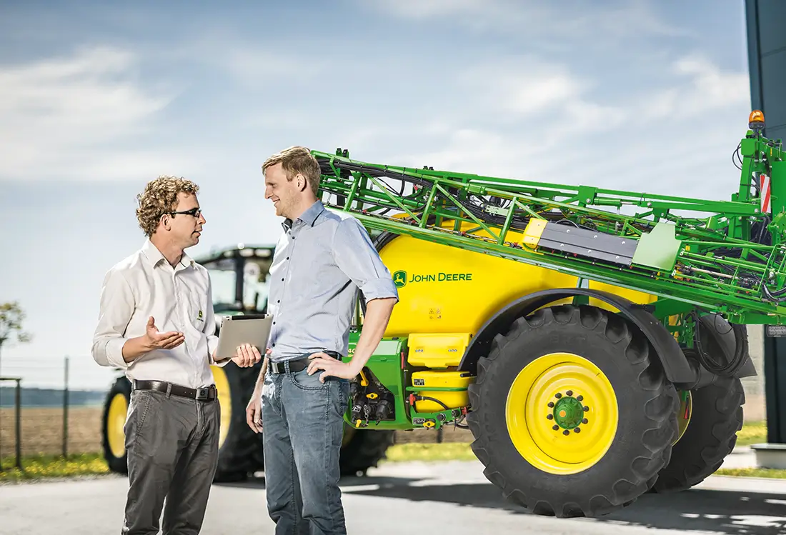 2 Männer unterhalten sich, im Hintergrund Traktor