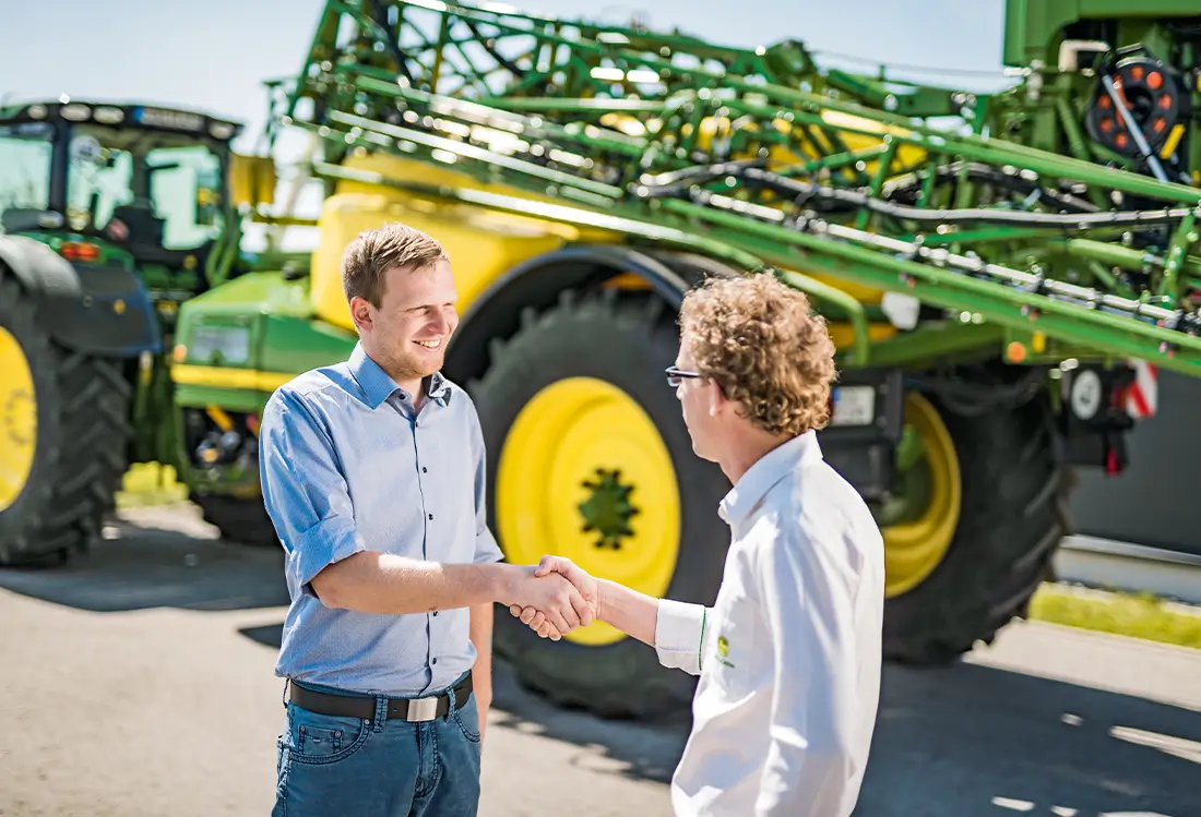 2 Männer schütteln die Hände vor Landmaschine